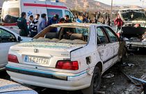 People stay next to destroyed cars after an explosion in Kerman, Iran, Wednesday, Jan. 3, 2024.