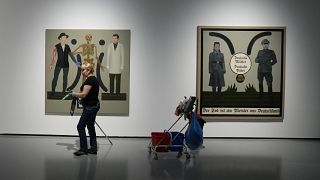 Two works by Polish artist Ignacy Czwartos on display at a 2021 exhibition. The painting on the right reads “German Mothers, German Fathers, Death Is A Master From Germany".