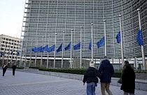 Pedestrians walk past as European Union flags flap in the wind at half staff, in remembrance of former European Commission President Jacques Delors, in front of European Union