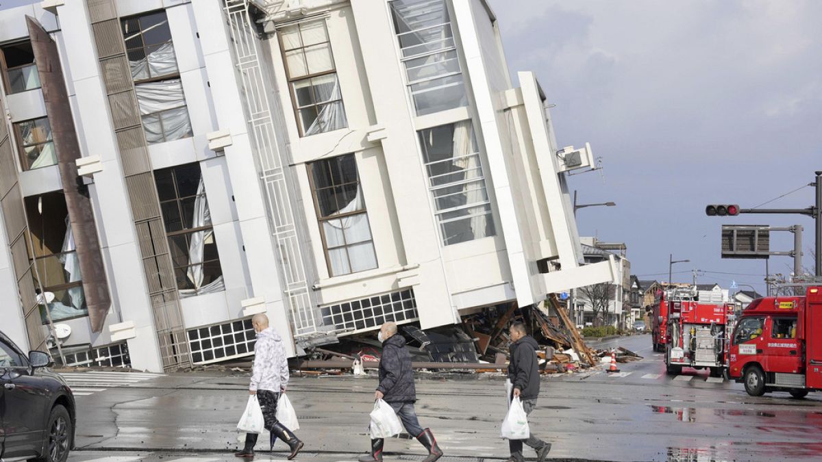 Wajima kentinde çöken bir binanın önünden geçen insanlar