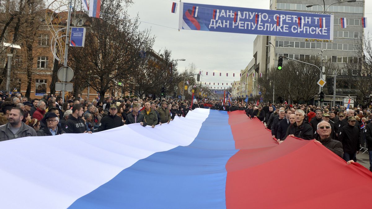 Sérvios da Bósnia marcham com uma bandeira sérvia gigante durante uma cerimónia por ocasião do "Dia da República Srpska" na cidade bósnia de Banja Luka, em 2022.