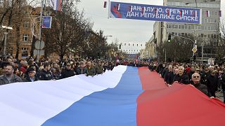 Sérvios da Bósnia marcham com uma bandeira sérvia gigante durante uma cerimónia por ocasião do "Dia da República Srpska" na cidade bósnia de Banja Luka, em 2022.