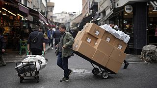 Two men pull trollies with goods in a street market in a commercial district in Istanbul, Turkey, Thursday, Dec. 21, 2023. Turkey's central bank hiked its key interest rate by