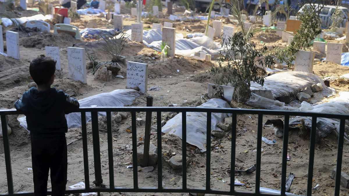 Uma criança palestiniana olha para os túmulos das pessoas mortas nos bombardeamentos israelitas na Faixa de Gaza e enterradas no recinto do Hospital Shifa, na Cidade de Gaza, a 31 de dezembro de 2023