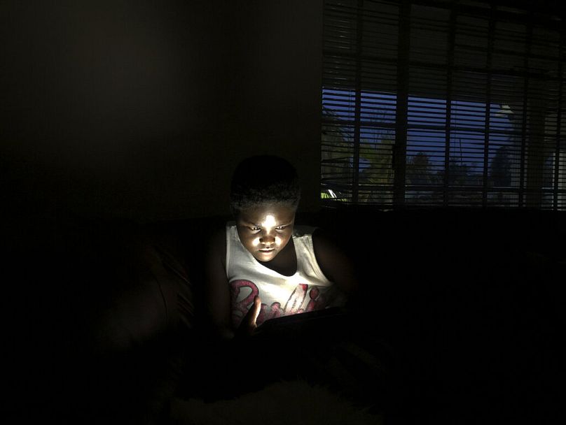 A young girl uses her mobile phone while charging it using solar power at a house in Harare, December 2019