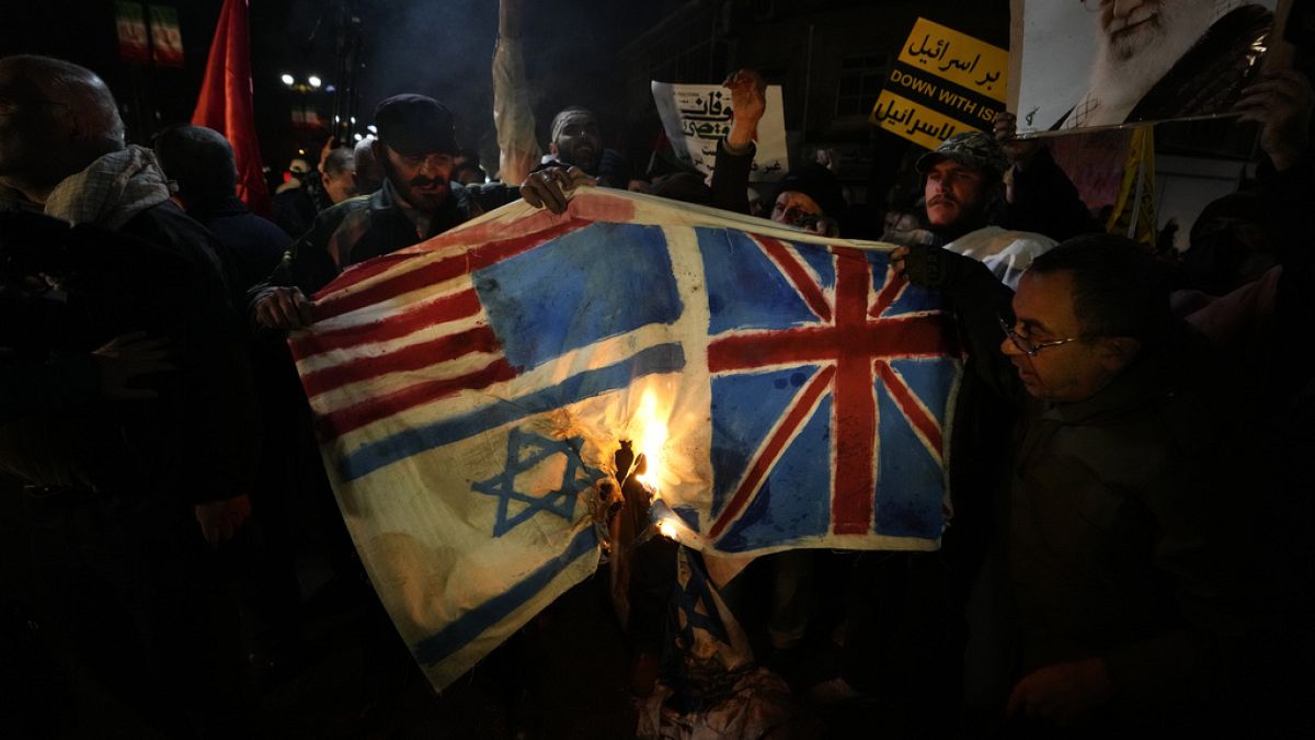 Iráni tüntetők brit, amerikai és izraeli zászlók ábrázolásait égetik el tüntetés közben, a brit nagykövetség előtt Teheránban, Iránban, 2024\. január 12-én, pénteken. 