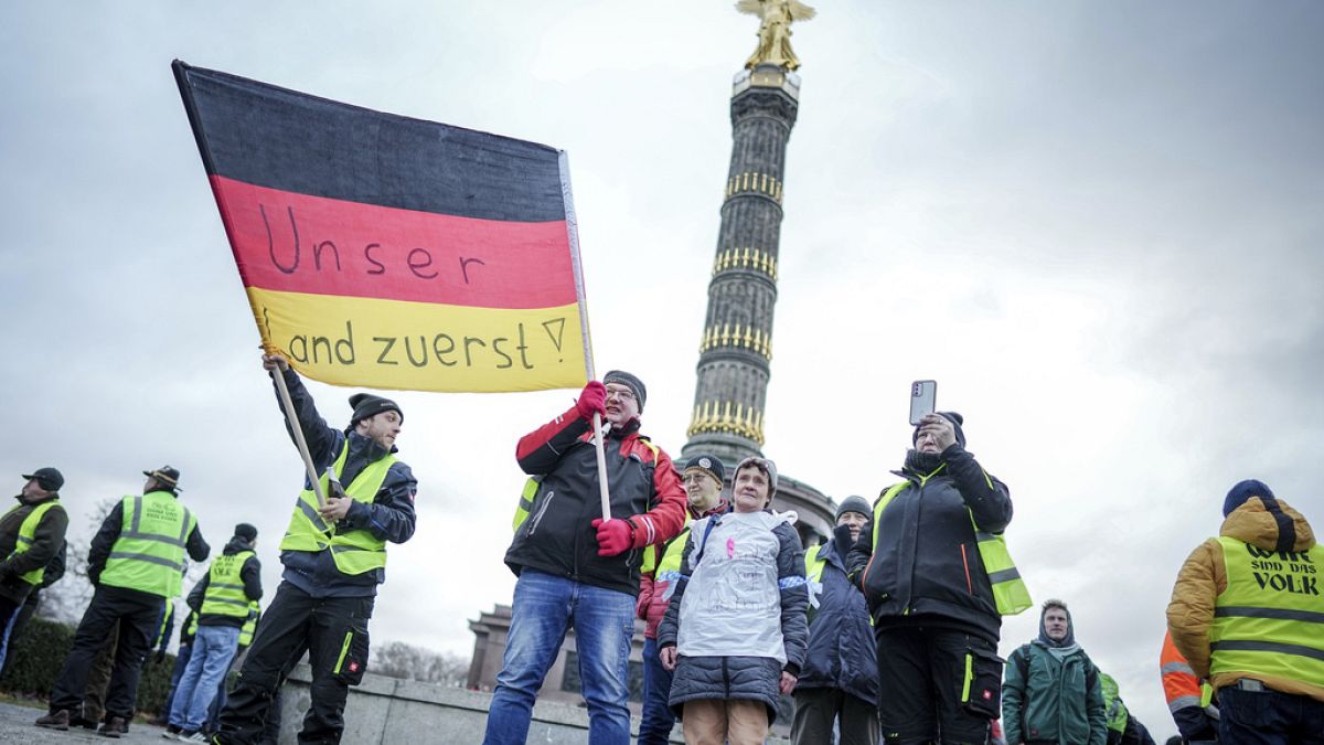Des agriculteurs brandissent un drapeau sur lequel est écrit en allemand "Notre pays d'abord" alors qu'ils protestent devant la Colonne de la Victoire, à Berlin, le lundi 15 janvier 2024. 15 janvier 2024.