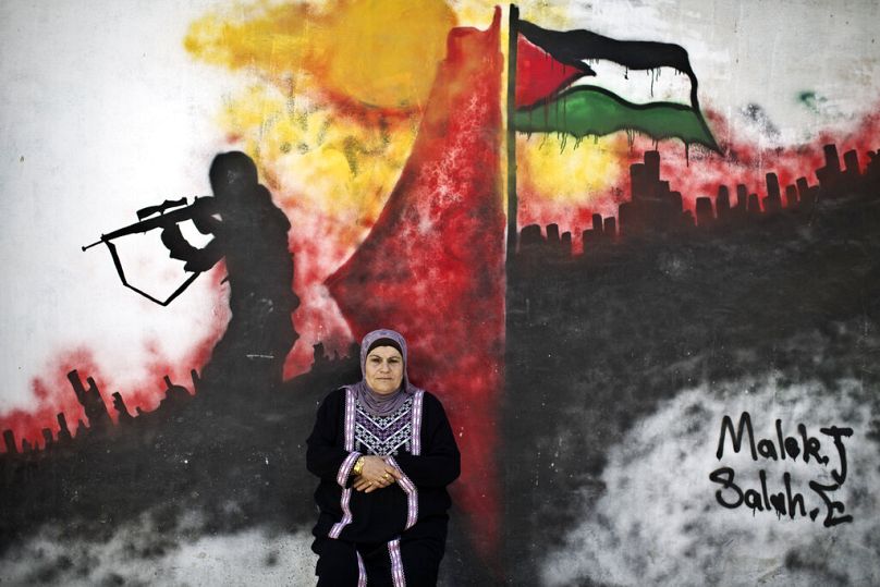 FILE - Palestinian refugee Layla Afaneh, 67, poses for a picture in front of a wall painted with a mural in the Kalandia refugee camp between Jerusalem and the West Bank, 2014