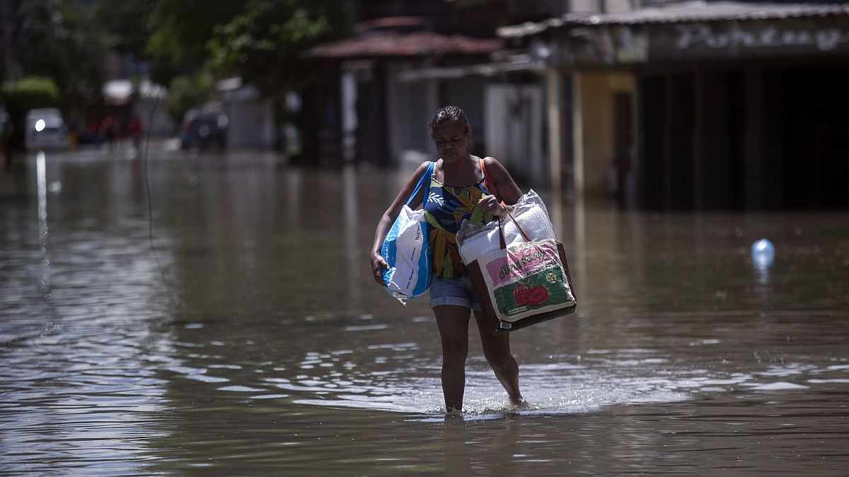 امرأة تحمل متعلقاتها عبر شارع غمرته المياه بعد هطول أمطار مميتة في بلفورد روكسو، البرازيل، الاثنين 15 يناير 2024.