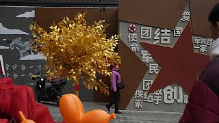 A women walks past a display depicting a golden tree and government propaganda calling for patriotism and unity between society and military at a mall in Beijing, Wednesday, J