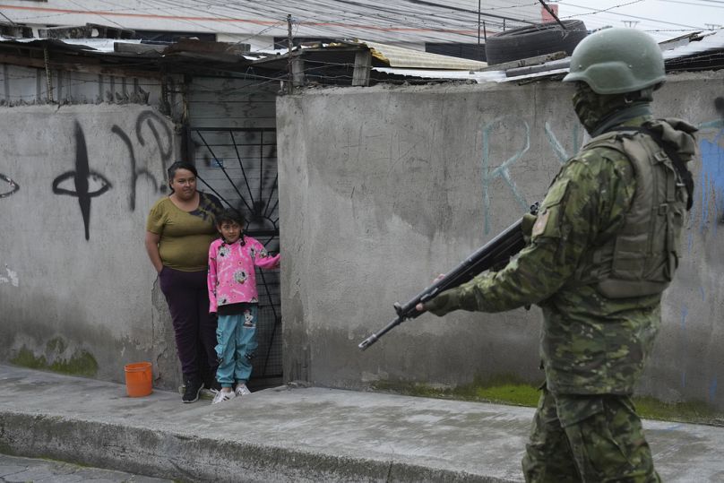 A soldier walks past residents on the south side of Quito, Ecuador, Friday, Jan. 12, 2024.