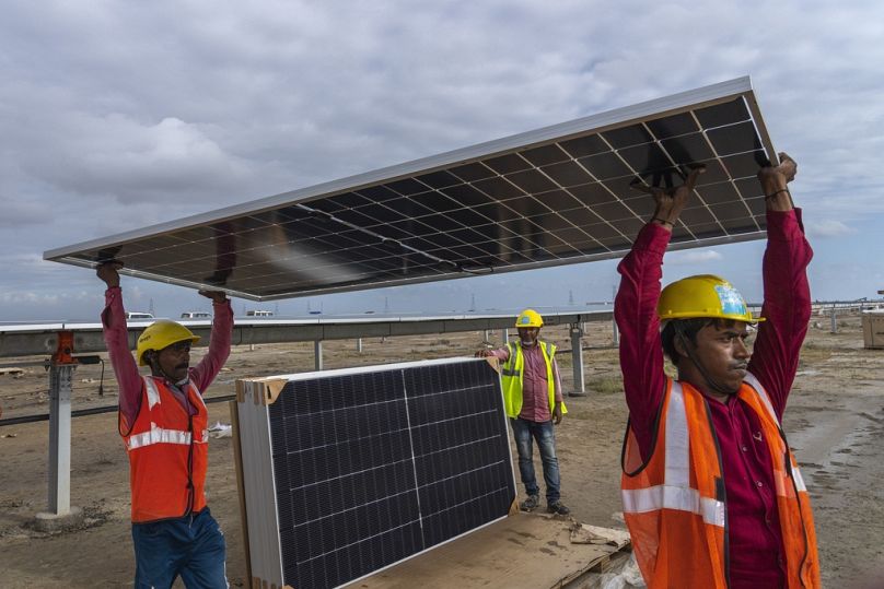 Arbeiter tragen ein Solarmodul zur Installation in den im Bau befindlichen Energiepark in der Salzwüste bei Khavda, Bundesstaat Gujarat, Indien, September 2023