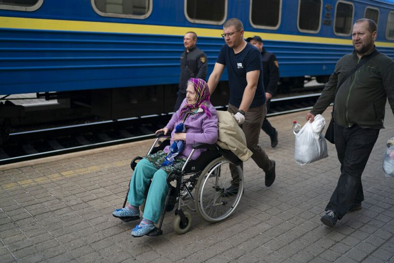 Volunteers help an elderly woman to board a train fleeing from the war in Severodonetsk and nearby towns at a train station in Pokrovsk, April 2022