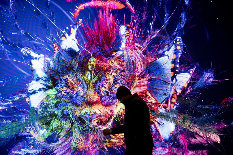 رجل يسير أمام شاشة بعمل فني تم إنشاؤه بالذكاء الاصطناعي للفنان الإعلامي رفيق أناضول، دافوس.