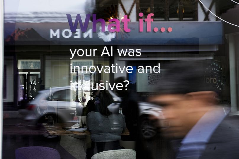 People reflected in a window of a building at the Davos Promenade with a slogan about AI alongside the World Economic Forum in Davos, January 2024