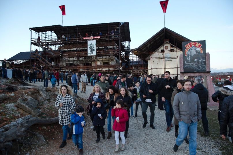 Koszovó albánok látogatják a prekazi mészárlás helyszínét 2017-ben; a háttérben a bal oldali Jashariék háza volt