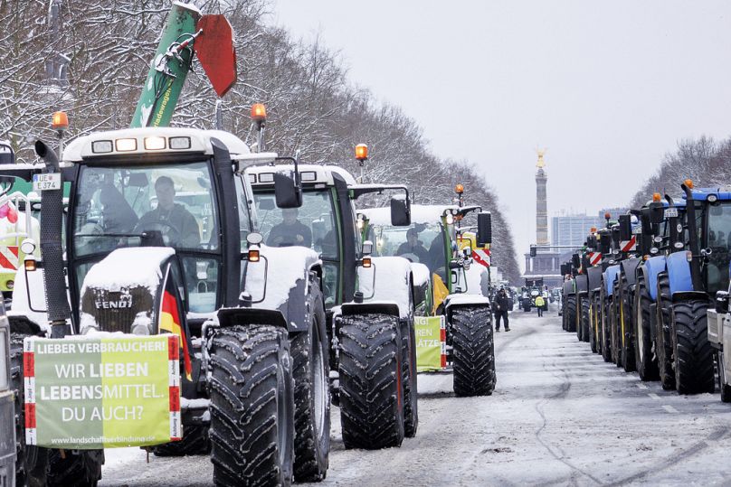A sign reading "We love food. You too?" is attached to a tractor that is driving towards the Brandenburg Gate with numerous other tractors during a protest in Berlin, Germany.
