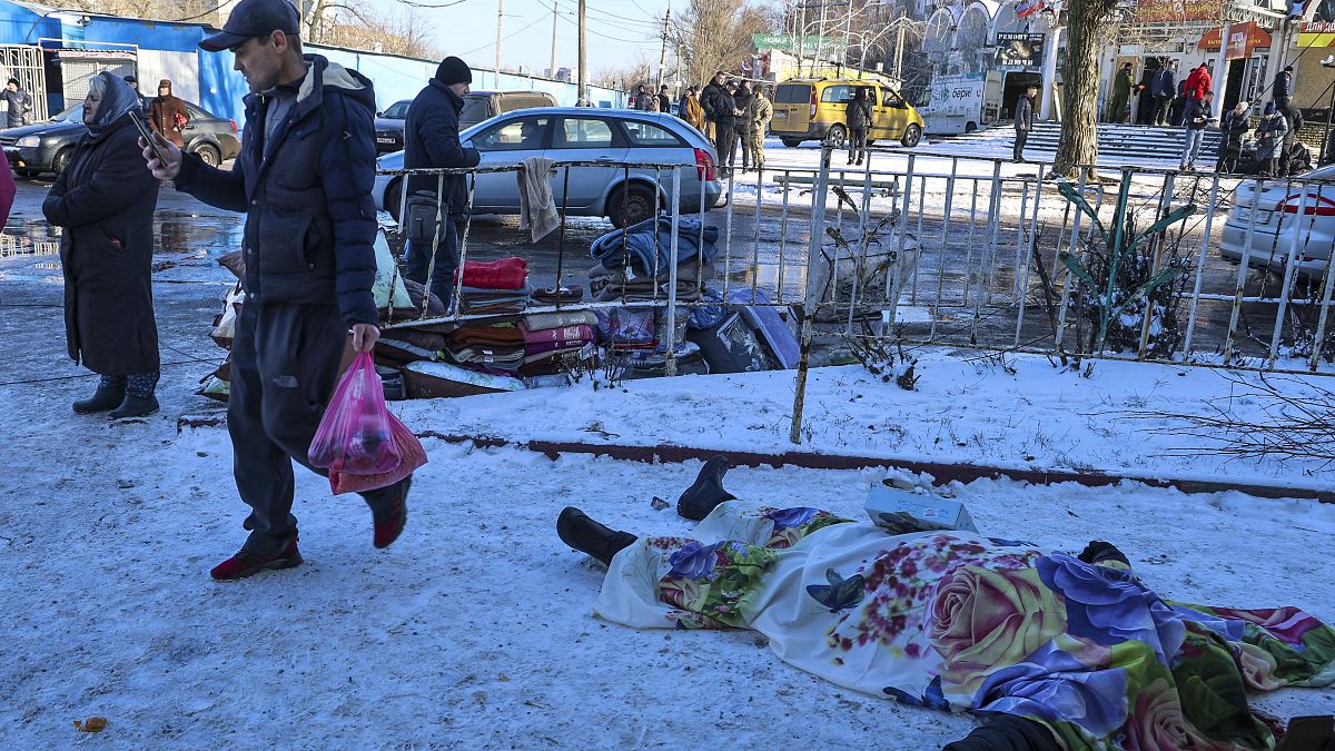 Pessoas passam por corpos de vítimas mortas durante o bombardeamento que as autoridades russas em Donetsk disseram ter sido conduzido pelas forças ucranianas