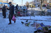Pessoas passam por corpos de vítimas mortas durante o bombardeamento que as autoridades russas em Donetsk disseram ter sido conduzido pelas forças ucranianas