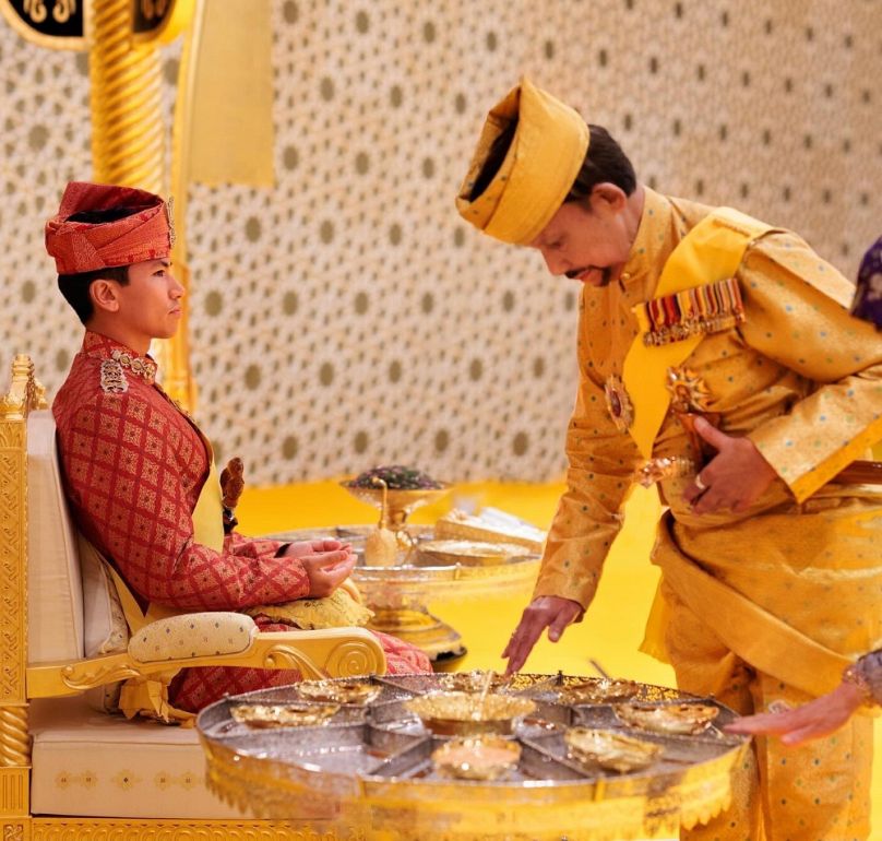 A szultán, talpig aranyban, megáldja élénkvörös maláji esküvői ruhába öltözött negyedik fiát