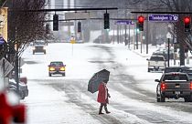 Un hombre cruza North Pine Street mientras los automovilistas circulan por una carretera cubierta de hielo y nieve en el centro de Florence, Alabama.