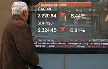 A passer-by stops to view a screen displaying markets news, with Paris' benchmark CAC-40 index showed on top,.