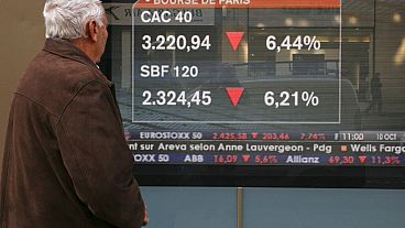 A passer-by stops to view a screen displaying markets news, with Paris' benchmark CAC-40 index showed on top,.