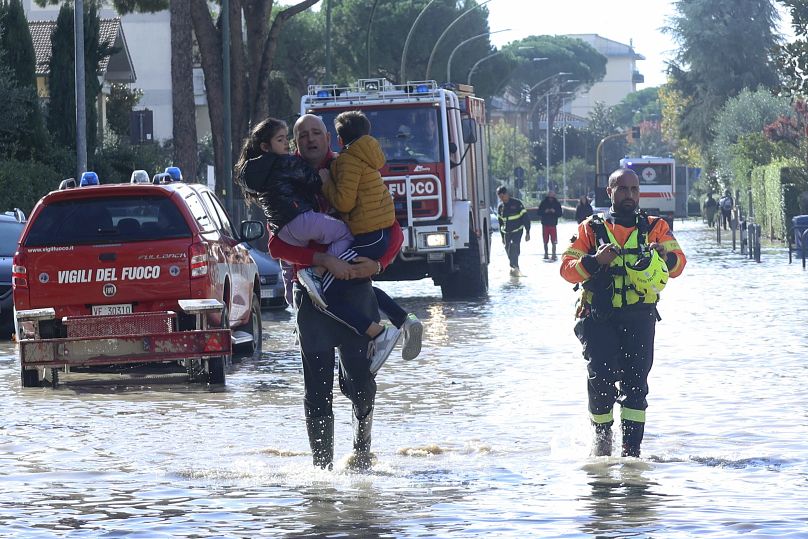 A man carries children through flood water, with emergency services at the scene after heavy rainfall, in Tuscany, Italy, November 2023.