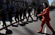 A protester in a Joker costume walks behind police leaving the area near Congress at the end of a protest during a national strike in Buenos Aires, 