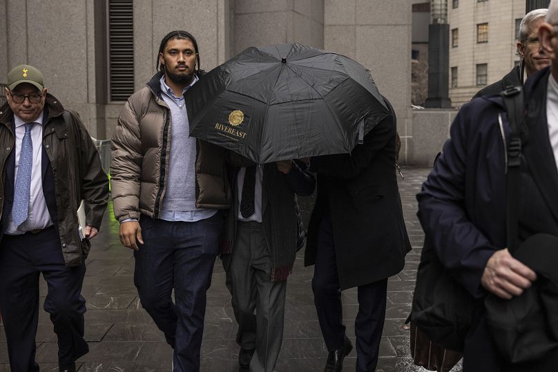 Joe Lewis, center, leaves Manhattan Federal court under cover of an umbrella after pleading guilty to insider trading charges, Wednesday, Jan. 24, 2024