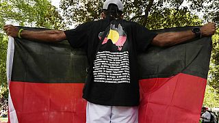 Un uomo protesta in Australia esponendo una bandiera aborigena