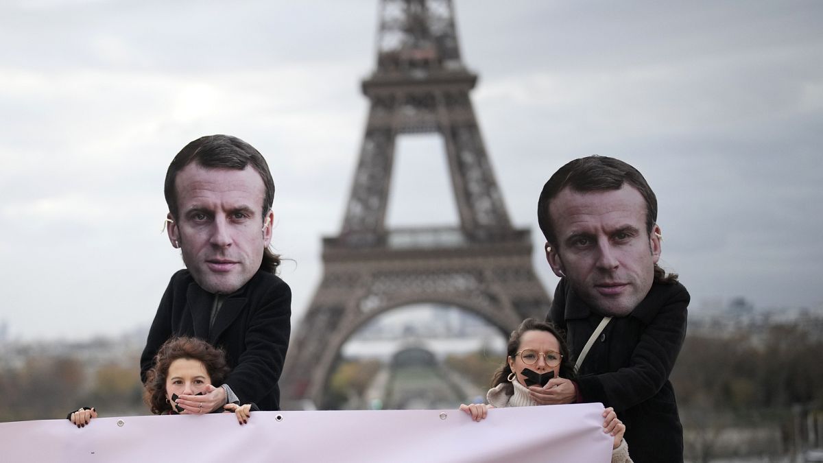 Attivisti con maschere di Emmanuel Macron mettono le mani su donne imbavagliate durante una manifestazione a Parigi, 24 novembre 2023