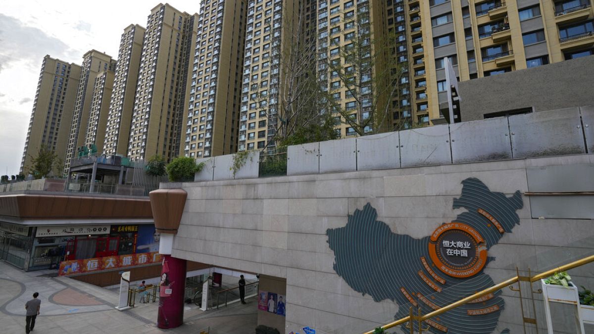 Bir adam 15 Eylül 2021'de Pekin'deki Evergrande şehir plazasında Evergrande geliştirme projelerini ve arkasındaki apartman binalarını gösteren bir Çin haritasının yanında yürüyor.