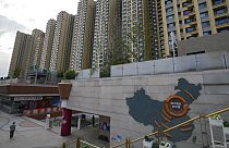 Bir adam 15 Eylül 2021'de Pekin'deki Evergrande şehir plazasında Evergrande geliştirme projelerini ve arkasındaki apartman binalarını gösteren bir Çin haritasının yanında yürüyor.