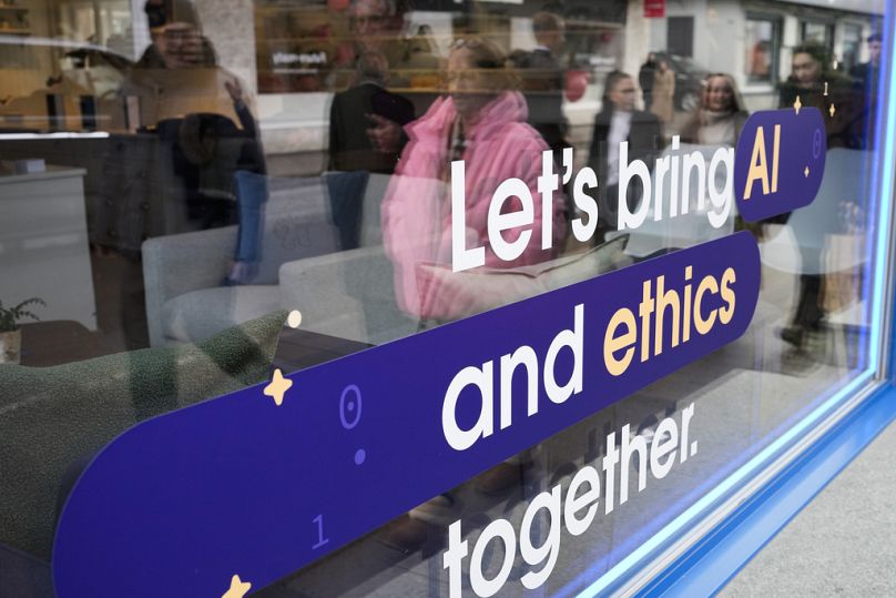 People reflected in a window of a building at the Davos Promenade with a slogan about AI alongside the World Economic Forum in Davos, January 2024