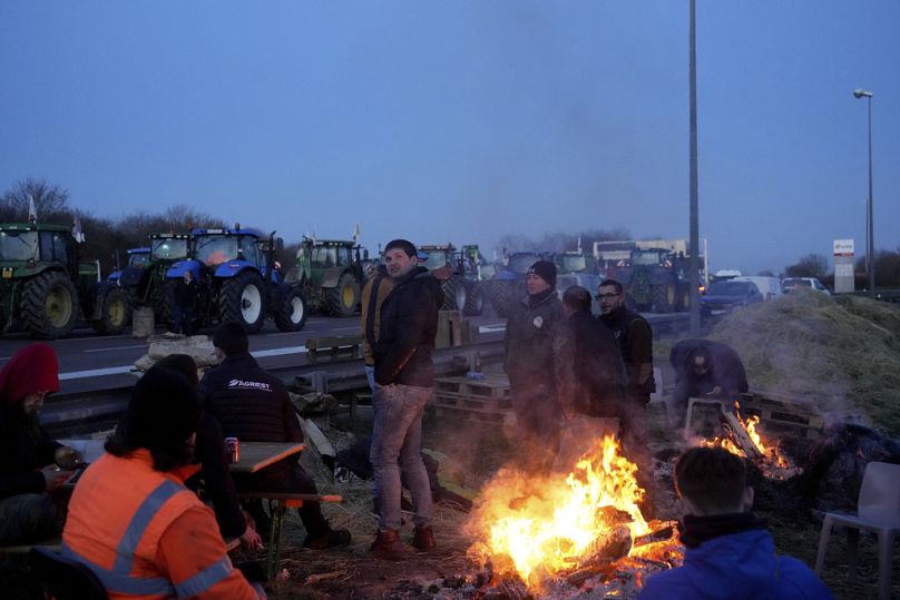 Farmers warm themselves around a bonfire as they block a highway with their tractors, in Ourdy, south of Paris, Wednesday