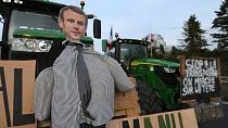 Un'effigie del presidente francese Emmanuel Macron viene vista su un trattore mentre gli agricoltori manifestano su un'autostrada.