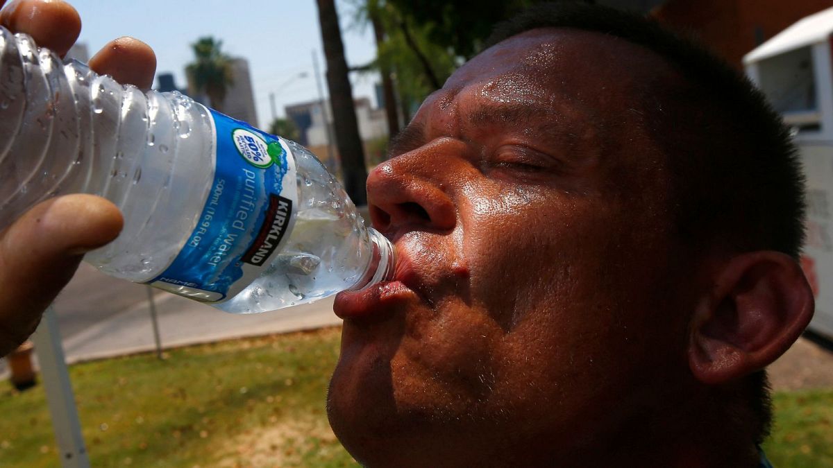 Мужчина пьет воду, пытаясь сохранить влагу и прохладу, когда температура воздуха достигла рекордных отметок в Фениксе, США, 2017 г.