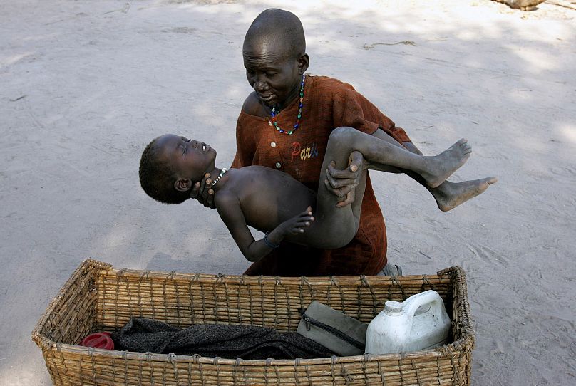 Eine Mutter legt ihren Sohn behutsam in einen Korb, um ihn in eine Klinik von Ärzte ohne Grenzen zu bringen, nachdem er an Malaria erkrankt ist, in Lankien, Südsudan, 2005.