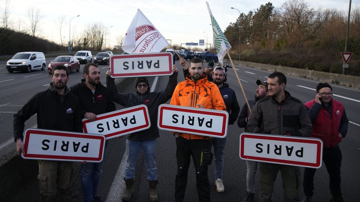 Gazdák tartják a fejjel lefelé fordított párizsi útjelző táblákat egy lezárt autópályán 2024. január 31-én, szerdán a Párizstól délre fekvő Chilly-Mazarinban.