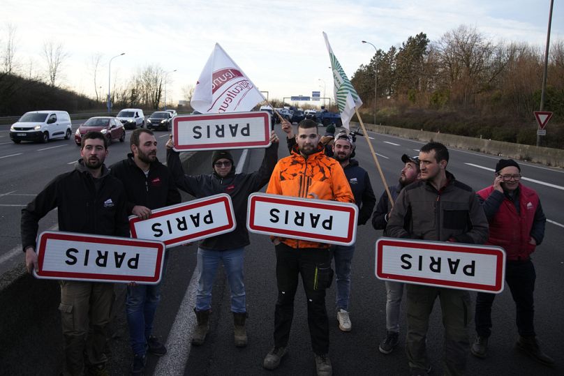 Farmers hold upside down road signs of Paris on a blocked highway, Wednesday, Jan. 31, 2024 in Chilly-Mazarin, south of Paris.
