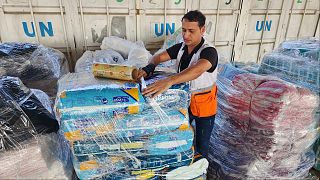 عمال الأمم المتحدة والهلال الأحمر يقومون بإعداد المساعدات للتوزيع على الفلسطينيين في مستودع الأونروا في دير البلح، قطاع غزة