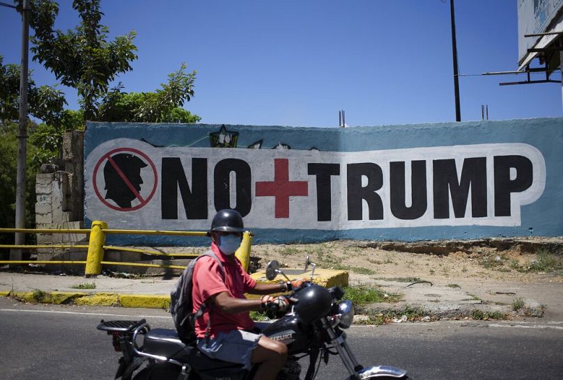 A man wearing a face mask as a precaution amid the spread of the new coronavirus passes a mural that in Spanish reads " No more Trump" in Caracas, Venezuela, Friday, March 27,