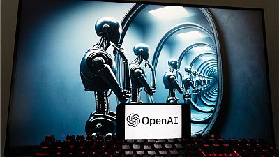 The OpenAI logo is seen displayed on a cell phone with an image on a computer screen generated by ChatGPT's Dall-E text-to-image model.