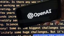 Le logo d'OpenAI apparaît sur un téléphone portable devant un écran affichant une partie du site web de l'entreprise.