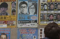 Körözötteket mutató poszter egy tokiói rendőrőrs előtt, középen felül Kirisima Szatosi fotójával 2024. február 2-án