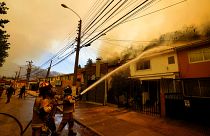 يقوم رجال الإطفاء برش المياه على المنازل بشكل وقائي بينما تشتعل حرائق الغابات في مكان قريب