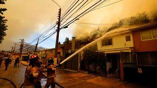 يقوم رجال الإطفاء برش المياه على المنازل بشكل وقائي بينما تشتعل حرائق الغابات في مكان قريب