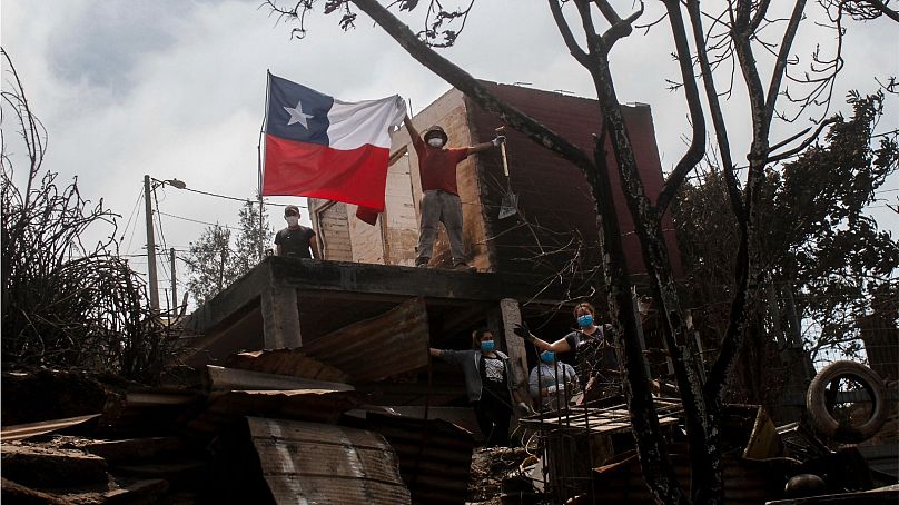 A resident poses displays a Chilean flag from a burnt-out house after forest fires reached his neighborhood in Vina del Mar, Chile, Sunday, Feb. 4, 2024.