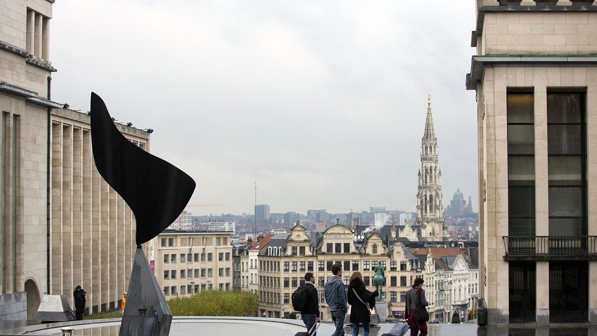 Des personnes marchent avec des bagages avec la ville de Bruxelles en toile de fond.